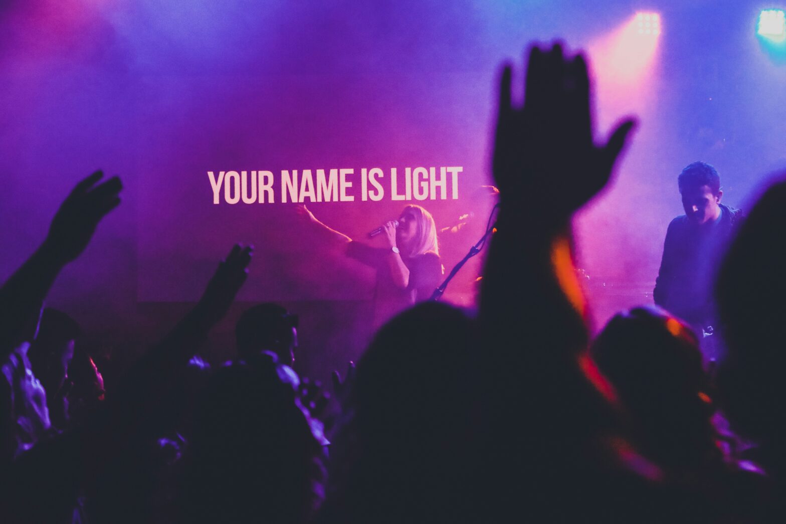 hand raised with lyrics "your name is light" on screen in the background